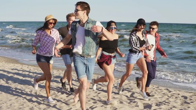Group of young hipster friends running together on a beach at the water's edge. Slowmotion shot