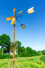 Fototapeta na wymiar Windmill for a water pump with blue sky and green trees