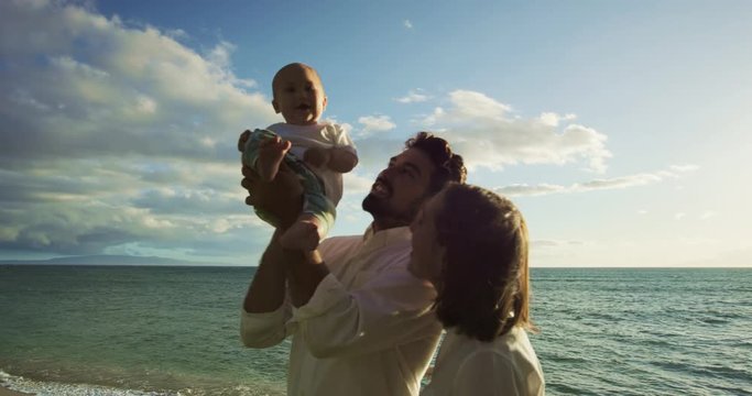Happy young parents walking with baby on the beach at sunset. Happy family on vacation