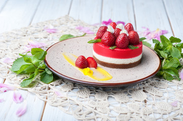Mini cake layered with cream and red strawberries on top on beautiful plate decorated with leaves of mint flowers and staying on napkin. Wooden white background. Food dessert healthy concepts.
