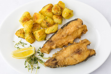 Fried fish garnished with potatoes, close up, top view at restaurant