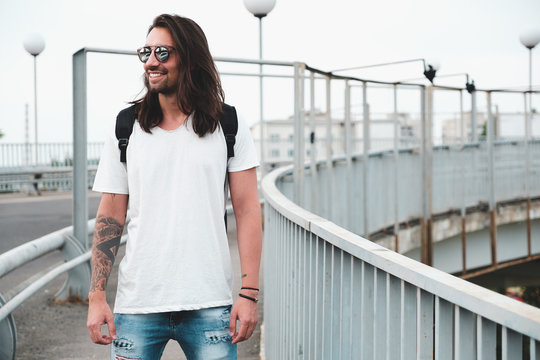Stylish hipster model with long hair lifestyle in the street. Dressed in a white T-shirt and torn blue jeans in the city