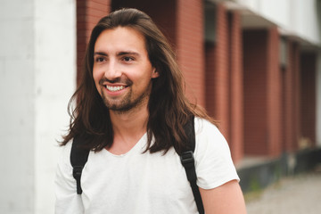 Stylish hipster model with long hair lifestyle in the street. Dressed in a white T-shirt and torn blue jeans in the city