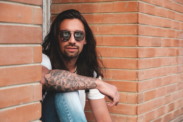 Stylish hipster model with long hair lifestyle in the street. Dressed in a white T-shirt and torn...