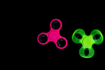 Pink and green Fidget Spinner in black background for stress release during work.