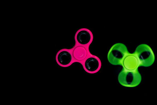 Pink and green Fidget Spinner in black background for stress release during work.