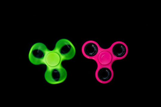 Pink and green Fidget Spinner in black background for stress release during work.