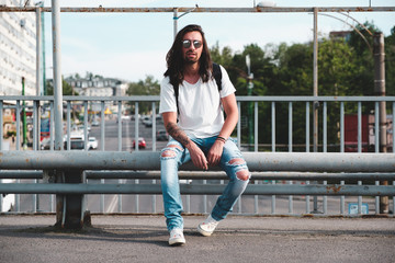 Stylish hipster model with long hair lifestyle in the street. Dressed in a white T-shirt and torn...