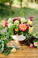 arts and crafts, wedding, decor, celebration, summer, nature concept - bunch of ornamental flowers like peonies, roses, avalanches and diathuses, decorated with verdure, placed in vase on wooden table