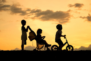 Silhouette of happy family, Little boy with small child in the stroller walking down the street and little boy riding bike having fun at sunset