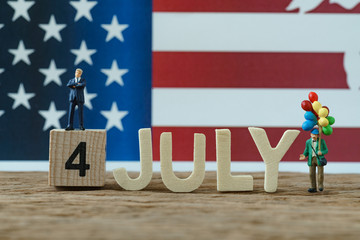 Independence day USA with miniature people old man holding balloon, businessman standing on wooden cube number 4 and alphabets JULY and United State national flag in the background