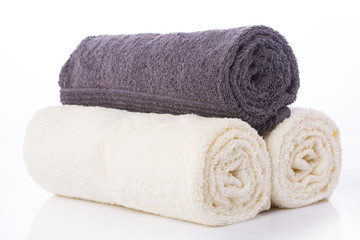 Two white towels and one gray rolled up on a roll on a white background