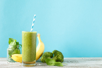Freshly blended green fruit smoothie in glass jar with straw. Turquoise blue background, copy space