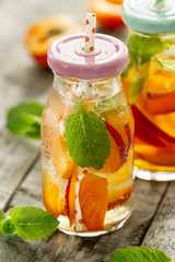Healthy tasty fresh refreshing detox water in bottles or jars with apricots, mint and ice on wooden background. Closeup. Healthy Life Concept.