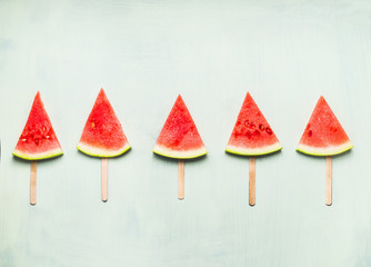 Watermelon slice popsicles on light turquoise background, top view. Healthy food and vegetarian eating concept