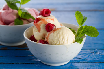Tasty appetizing vanilla and strawberry ice cream with jam in bowls on wooden table. Closeup.
