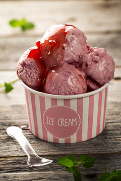 Tasty appetizing vanilla strawberry ice with jam in pink paper cup on wooden table. Closeup.