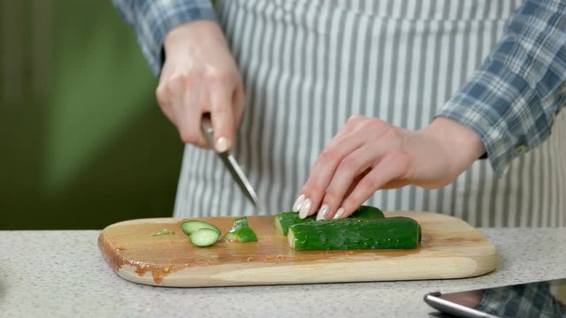 Female hands cutting cucumber. Green vegetable on wooden board. Facts about vegetables.