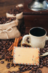 Cup of coffee with sack full of roasted coffee beans and coffee mill on wooden table