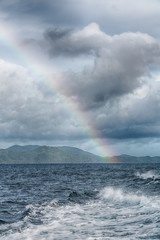 the rainbow from  ocean and island in background