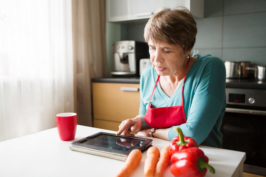 Elegant Elderly Woman Using  Tablet In The Kitchen