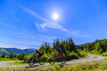 Mountain biking women and man riding on bikes in summer mountains forest landscape. Couple cycling outdoor sport activity.