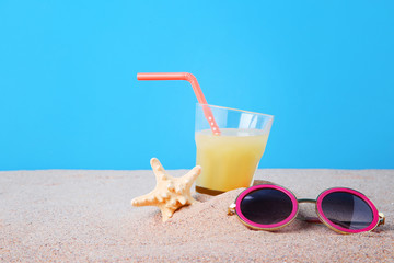 Fototapeta na wymiar Pink sunglasses with glass of juice and starfish on the beach sand