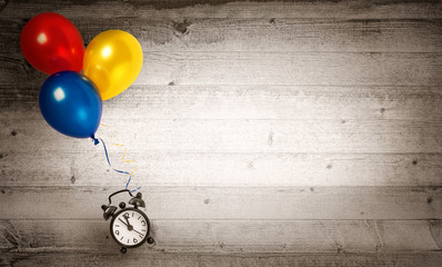 Clock flying with several balloons on a wooden background