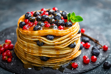 Pancakes with fresh berries and maple syrup on dark background, closeup
