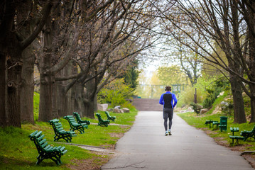 View from back. Young man with headphones running in spring park nature and listening music. Helth concept of life