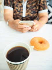 Woman using smart phone with eating coffee and donut