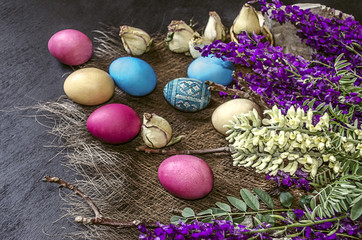 Fototapeta na wymiar Colored Easter eggs near the bouquet of wild flowers,buds of roses on a black background