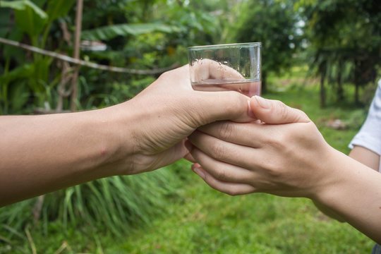 Man hand giving glass of fresh water to women in the park.