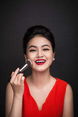 Obraz premium Cosmetic powder brush. Asian woman applying blusher on her cheeks with perfect make-up and red lips