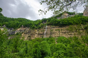 Foto op Canvas Waterfall on a high rock mountain. Cloudy landscape wallpaper with green Caucasus forest. Guam Gorge © Boris