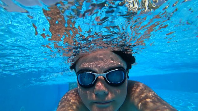 Portrait of the happy teenager swimming underwater and smiling to camera