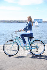 Fototapeta premium Young smiling girl with bicycle on embankment