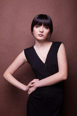 Beautiful woman in long black dress on brown background in studio photo. Beauty and fashion. Model test