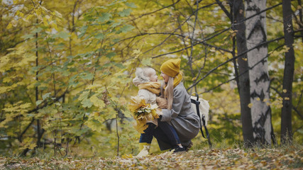 Mother and daughter together among yellow leaves in autumn park