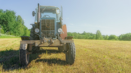 Fototapeta na wymiar red old rusty tractor in a field of mown grass against a forest background in good weather