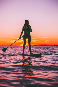 Girl stand up paddle boarding on a quiet sea with warm sunset colors