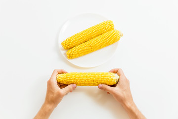 Boiled corn on a plate and in hand on white background. Flat lay. Top view. Natural food
