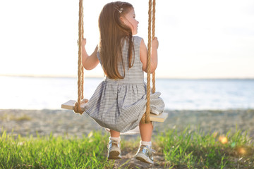 Cute little girl playing on swing near river