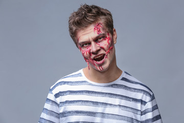 Young man with Halloween makeup on grey background