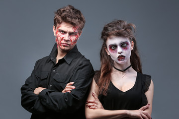 Young man and woman with Halloween makeup on grey background