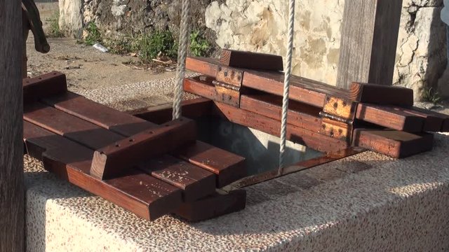 A person inserts two buckets into a water well to draw water with the help of a rope and a pulley.