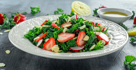 Healthy kale salad with strawberries and almond in a white plate