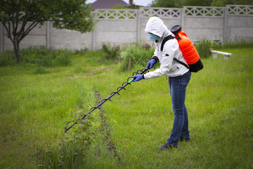 Red garden sprayer behind the worker in a white jacket and jeans, with a fence background.