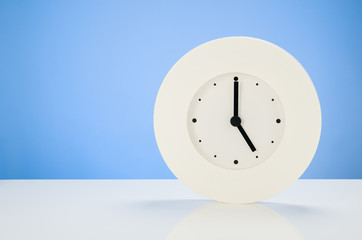 White analog modern clock on white table with blue seamless background
