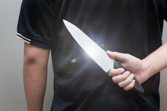 Closeup of a young man hand, holding knife behind his back and waiting for a woman to attack, concept of danger, stress, unfulfillment, risk.